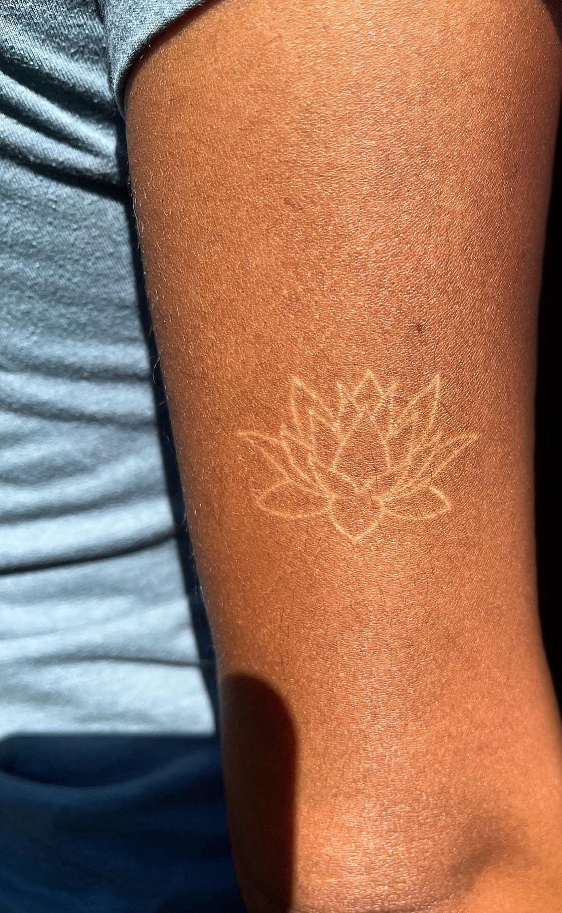 White ink lotus flower tattoo on a person's dark brown skin arm.