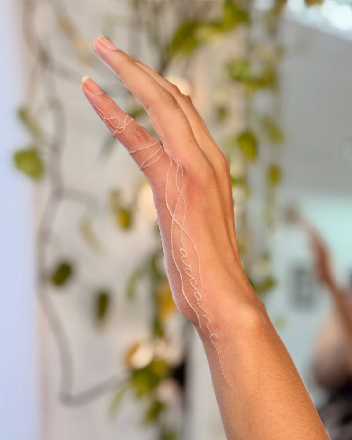 Hand and wrist with a delicate white ink tattoo of cursive text.