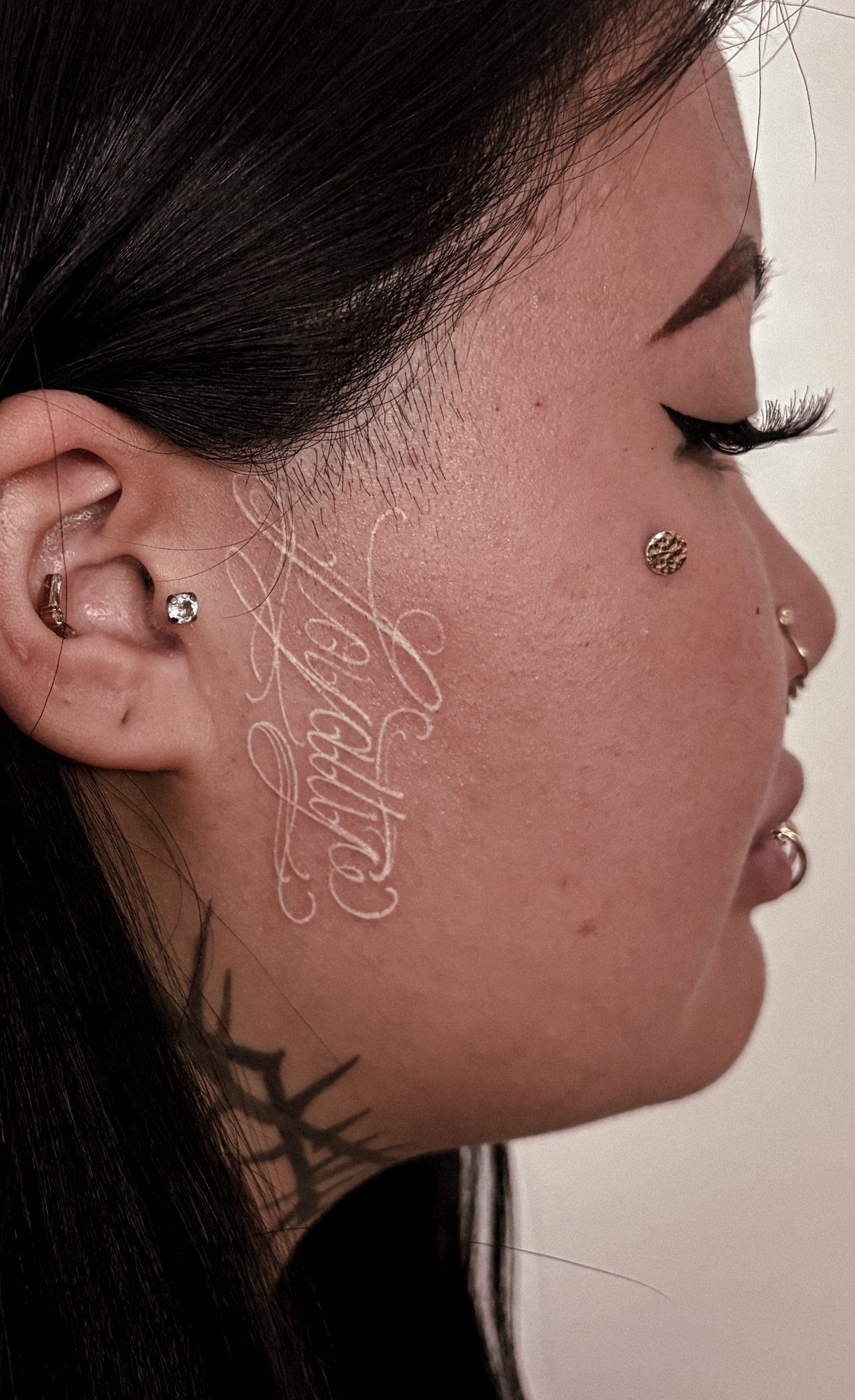 White ink script tattoo on the cheek of a person with dark skin