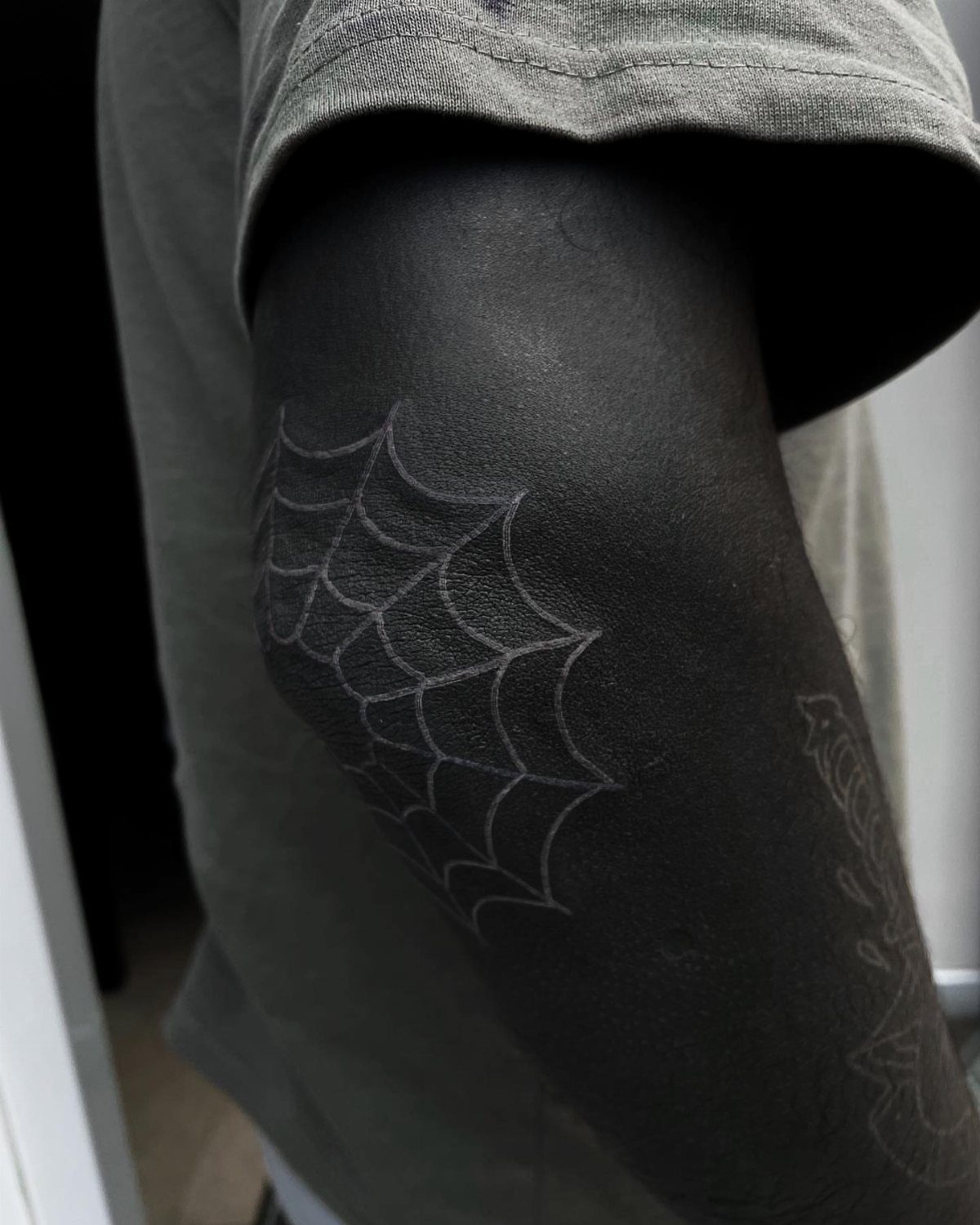White ink spiderweb tattoo on the elbow of a person with dark skin.