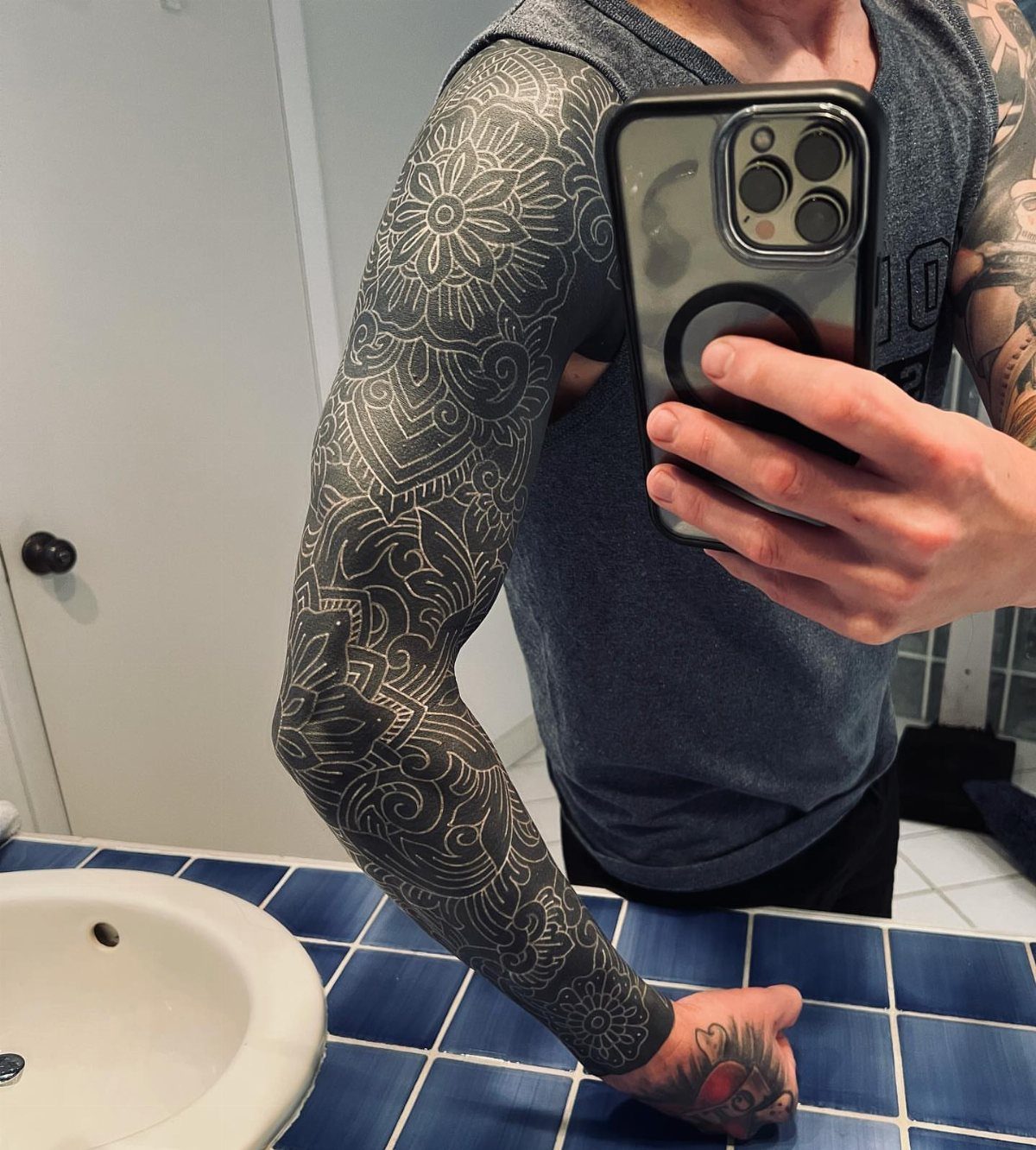 Arm with white ink floral patterns tattooed over a solid black sleeve background