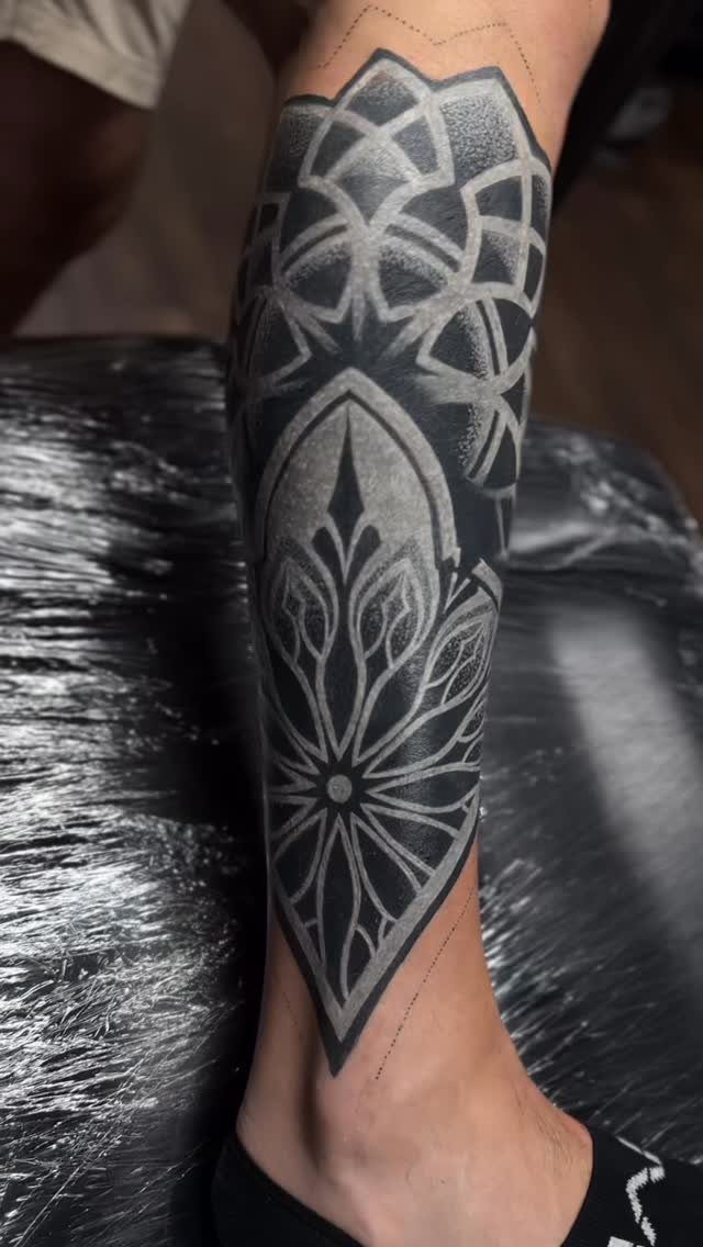 White geometric tattoo patterns layered over a solid blacked-out lower leg and ankle.