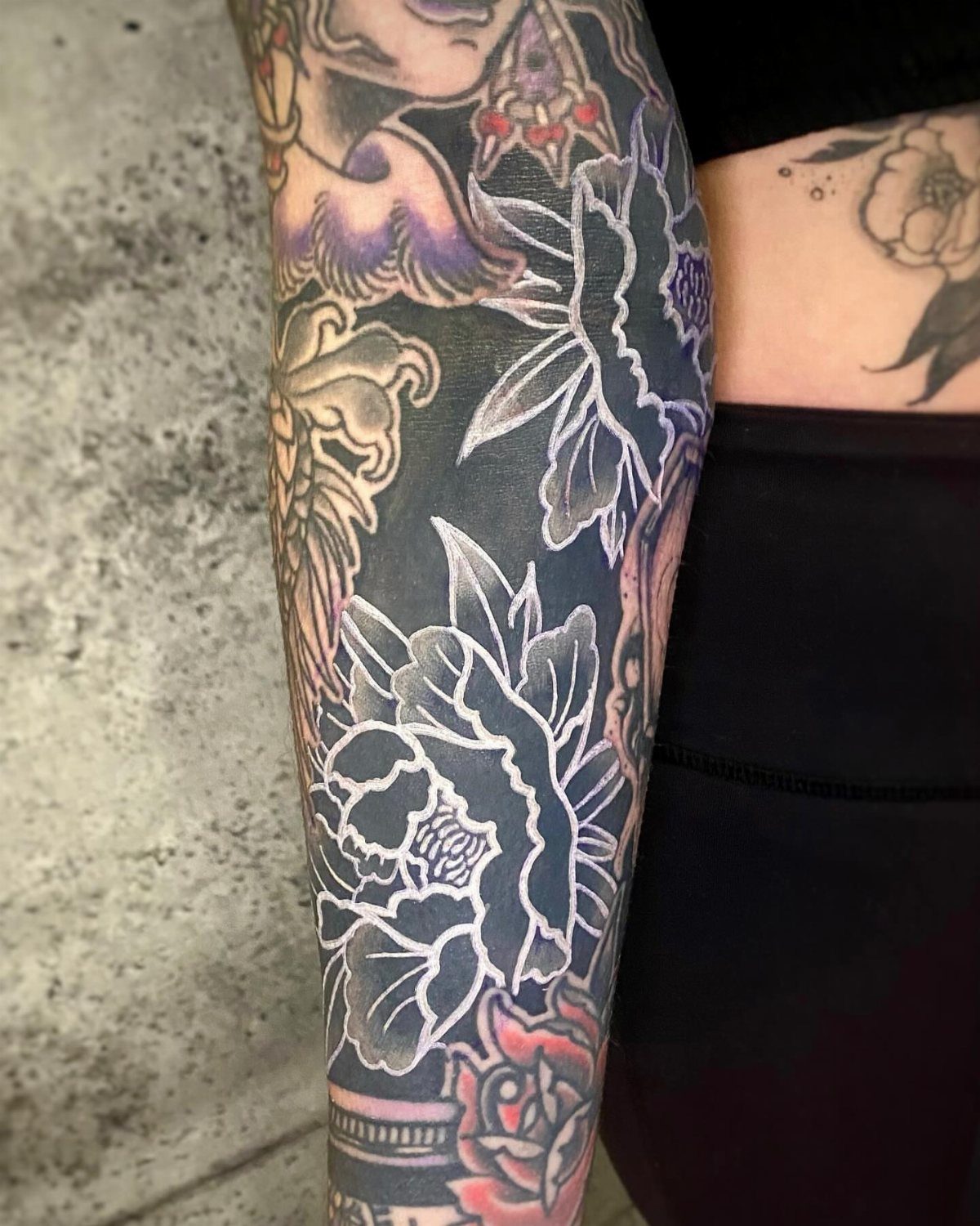 Arm tattoo with white ink floral outlines layered over a solid black background.