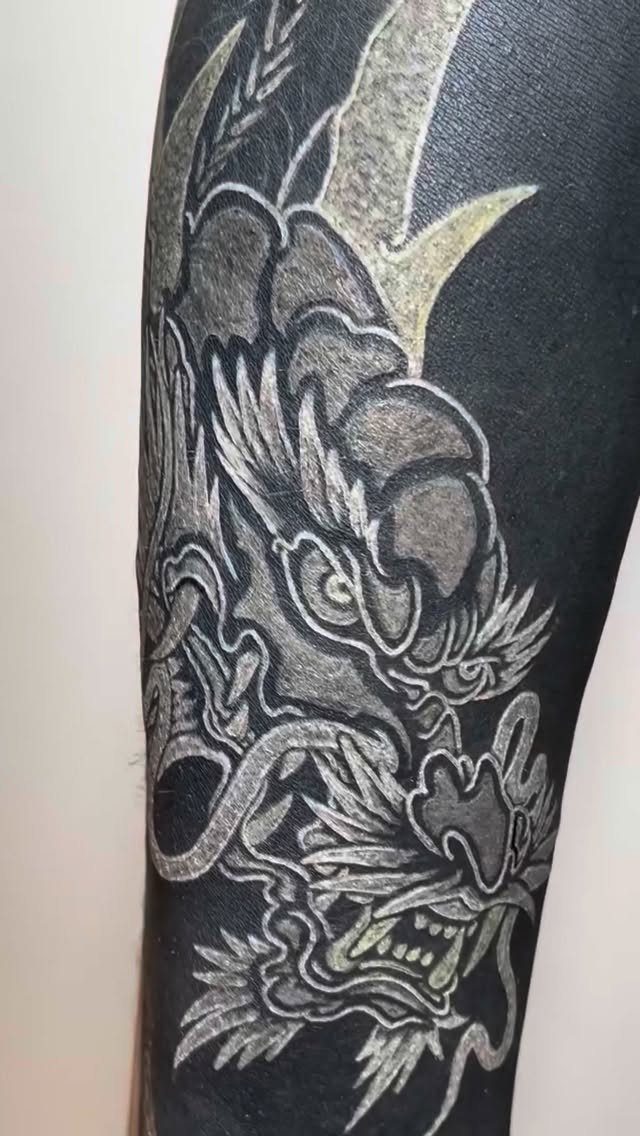 Dragon head tattoo created with white ink over a solid black blackout background.