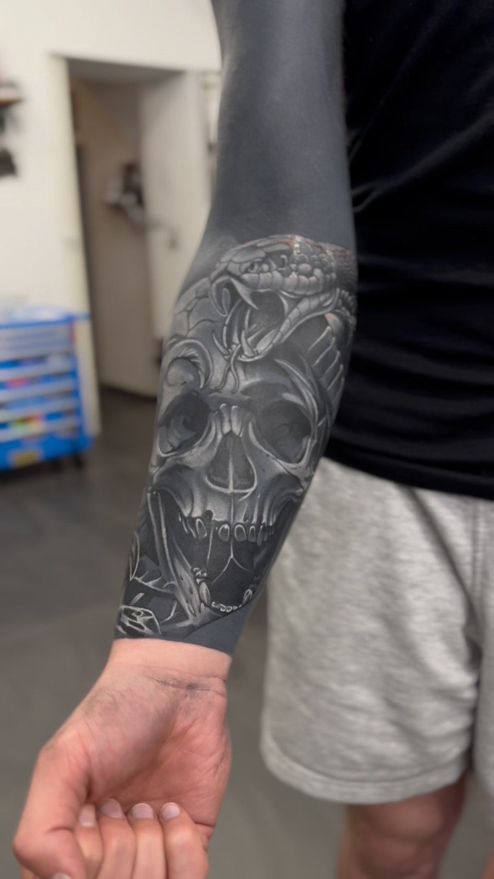 Blackout tattoo sleeve on an arm featuring a detailed white ink skull design.