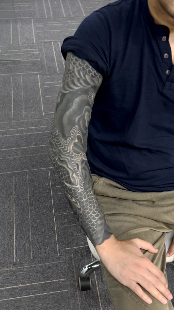 Full sleeve tattoo with white ink patterns over a solid black background on an arm.